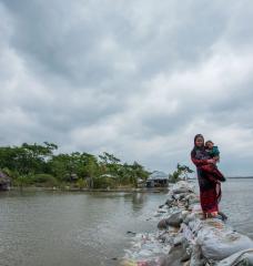 For the coastal country of Bangladesh, once-in-a-century storm tides could strike every 10 years — or more often — by the end of the century, scientists report. In this photo, a Bangladeshi woman and child walk over the top of a sandbag embankment in Khulna on May 4, 2019.